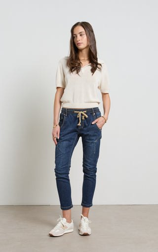 Woman wearing a Dark Blue Indigo jogger jeans with elasticated wait and drawstring standing against a white background