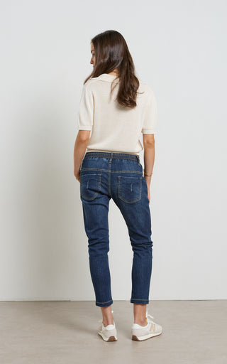 Woman wearing a Dark Blue Indigo jogger jeans with elasticated wait and drawstring standing against a white background