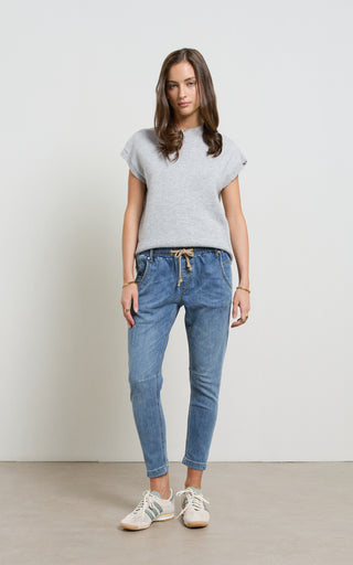Woman wearing a blue jogger jeans with elasticated wait and drawstring standing against a white background