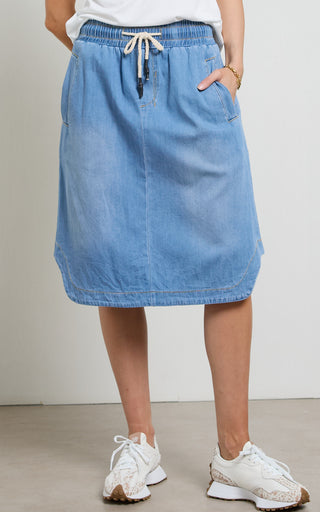 Woman wearing a Mid Blue light weight Denim Skirt with elasticated wait and drawstring standing against a white background