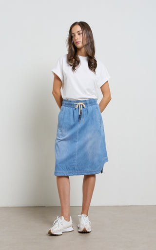 Woman wearing a Mid Blue Denim Skirt with elasticated wait and drawstring standing against a white background
