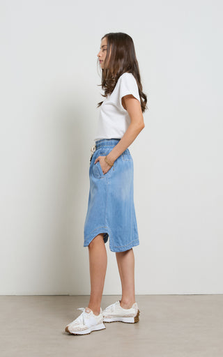 Woman wearing a Mid Blue light weight Denim Skirt with elasticated wait and drawstring standing against a white background