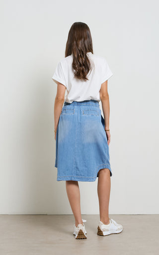 Woman wearing a Mid Blue light weight Denim Skirt with elasticated wait and drawstring standing against a white background