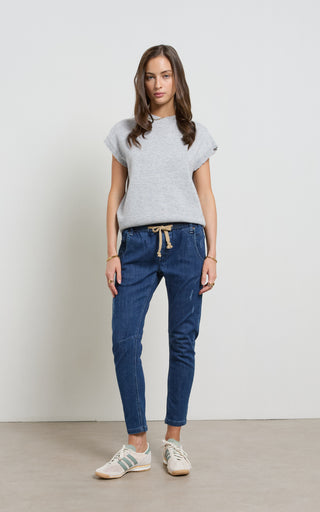 Woman wearing a Dark Denim jogger jeans with elasticated wait and drawstring standing against a white background