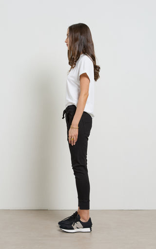 Woman wearing a white t-shirt and black pants standing against a plain white wall.