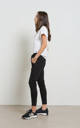 Woman wearing a white t-shirt and black pants against a plain background