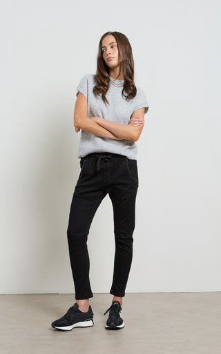 Person wearing a gray t-shirt and black pants standing against a white wall.