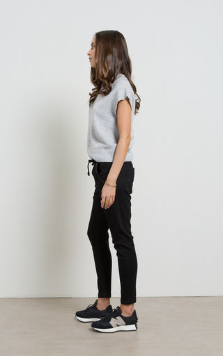 Woman wearing a light gray t-shirt, black pants, and black sneakers against a white background