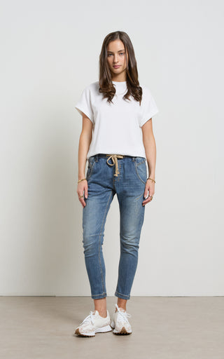 Woman wearing a Mid Blue Denim jogger jeans with elasticated wait and drawstring standing against a white background