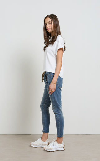 Woman wearing a Mid Blue Denim jogger jeans with elasticated wait and drawstring standing against a white background