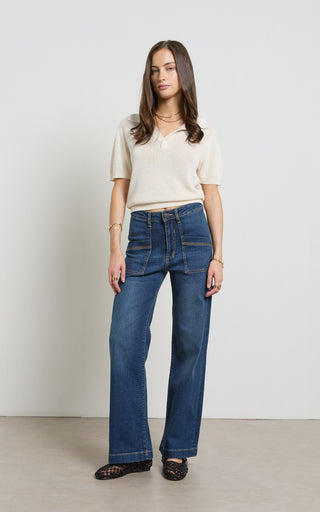 Woman wearing a wide leg dark blue stretch denim jeans standing against a white background