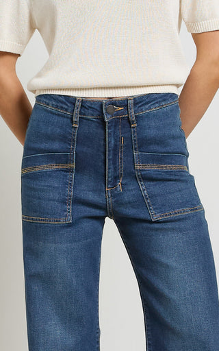 Woman wearing a wide leg dark blue stretch denim jeans standing against a white background