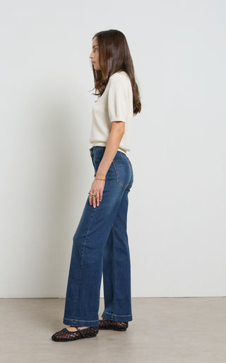 Woman wearing a wide leg dark blue stretch denim jeans standing against a white background