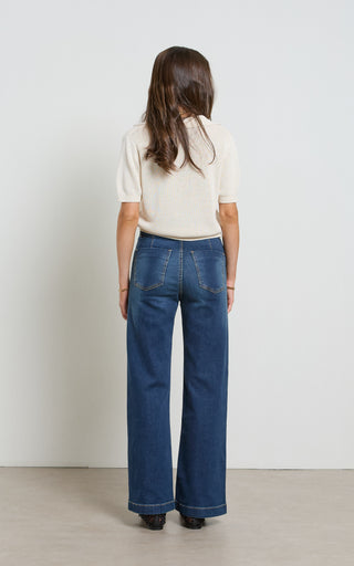 Woman wearing a wide leg dark blue stretch denim jeans standing against a white background