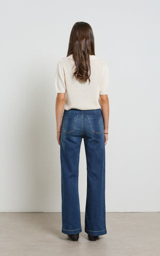 Woman wearing a wide leg dark blue stretch denim jeans standing against a white background