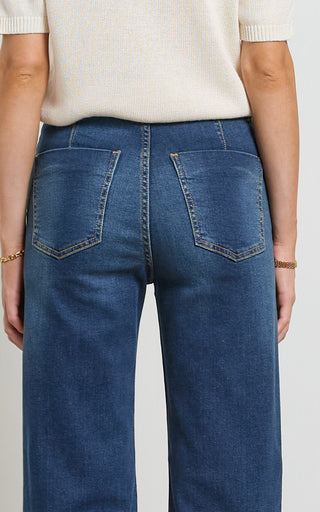 Woman wearing a wide leg dark blue stretch denim jeans standing against a white background