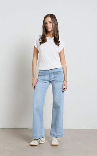 Woman wearing a wide leg light blue stretch denim jeans standing against a white background