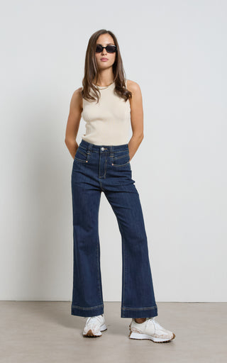 Woman wearing a wide leg Dark Indigo stretch denim jeans standing against a white background