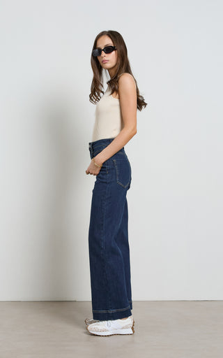 Woman wearing a wide leg Dark Indigo stretch denim jeans standing against a white background