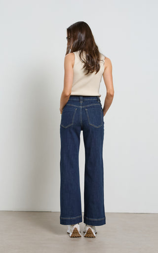 Woman wearing a wide leg Dark Indigo stretch denim jeans standing against a white background