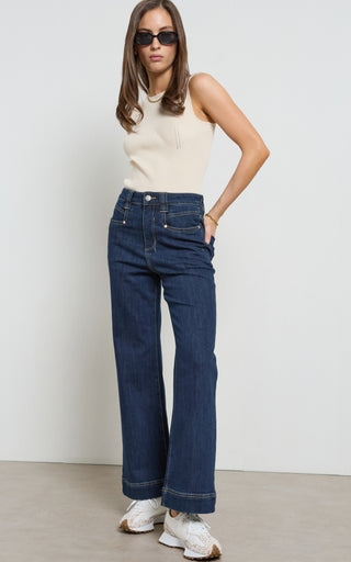 Woman wearing a wide leg Dark Indigo stretch denim jeans standing against a white background