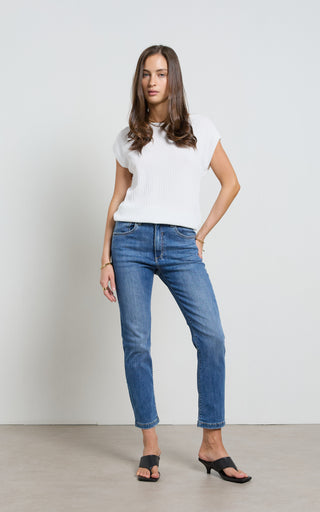 Woman wearing a straight leg Mid blue stretch denim jeans standing against a white background